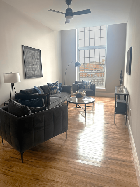 A living room with a black couch and a ceiling fan.
